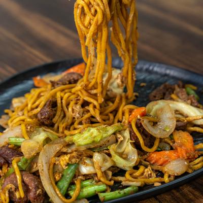 Stir fried noodles with vegetables on a black plate.