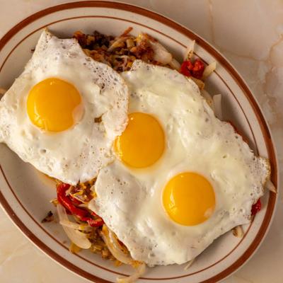 Three sunny side up eggs served over hash browns and vegetables.