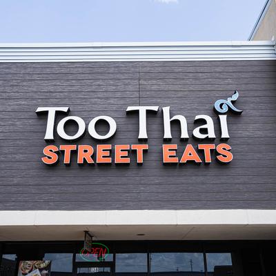 Exterior sign of Too Thai Street Eats restaurant on a dark wood facade.