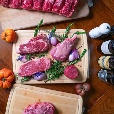 Assorted raw steaks on cutting boards with rosemary and onions, with bottles of red wine.