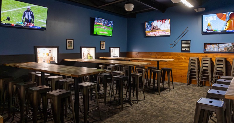 Seating area, tables with bar stools and large TV screens on the walls