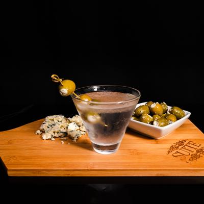 Martini cocktail, served with cheese and cheese stuffed olives on a wooden board.