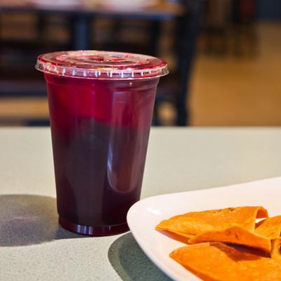Dark red juice served in a clear plastic cup alongside a plate of food.