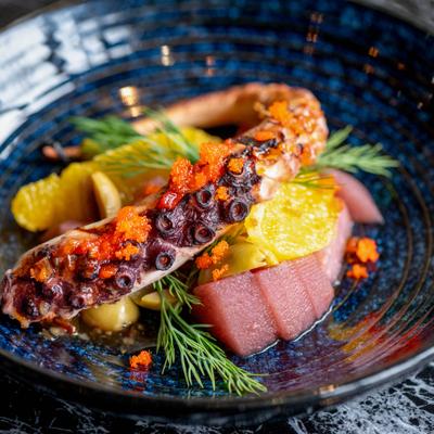 Grilled octopus served with vegetables on a blue plate.