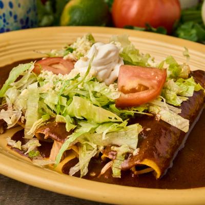 Enchiladas in a mole poblano sauce, topped with shredded lettuce, tomatoes, and sour cream.