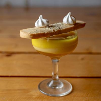 Layered custard dessert in a coupe glass, topped with biscotti and two small meringue cookies.