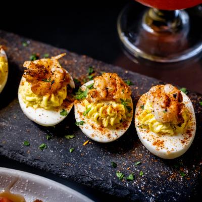 Deviled eggs topped with seasoned shrimp, garnished with herbs and paprika.