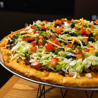 Pizza with ground beef, lettuce, tomato, olives, scallions, jalapenos, and cheese.
