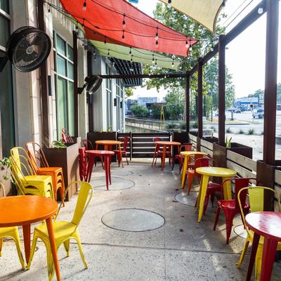 Colorful outdoor patio with bright tables, chairs, and overhead shade sails.