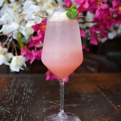 A spirit free cocktail sits on a wooden table with white and pink flowers in the background.