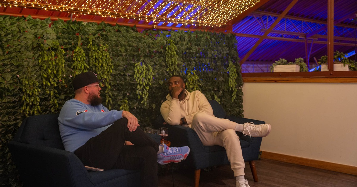 Two people sitting in armchairs by a greenery decorated wall and conversing