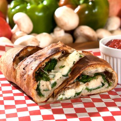 Cheesy calzone with spinach and chicken, fresh vegetables in the background.