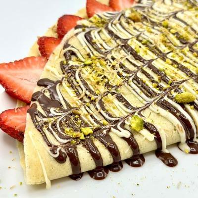 Strawberry crepe drizzled with chocolate and white sauce, topped with crushed pistachios.