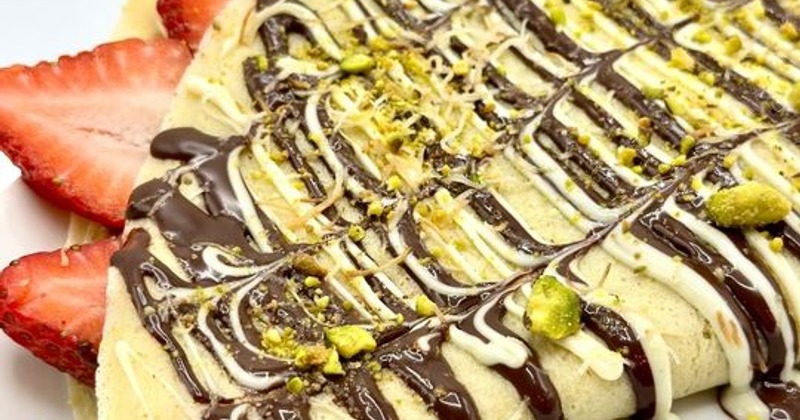 Strawberry crepe with chocolate and white sauce drizzle and crushed pistachios