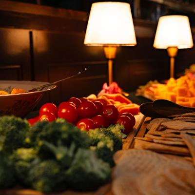 A warmly lit buffet table displays vibrant vegetables, cheese, and crackers.
