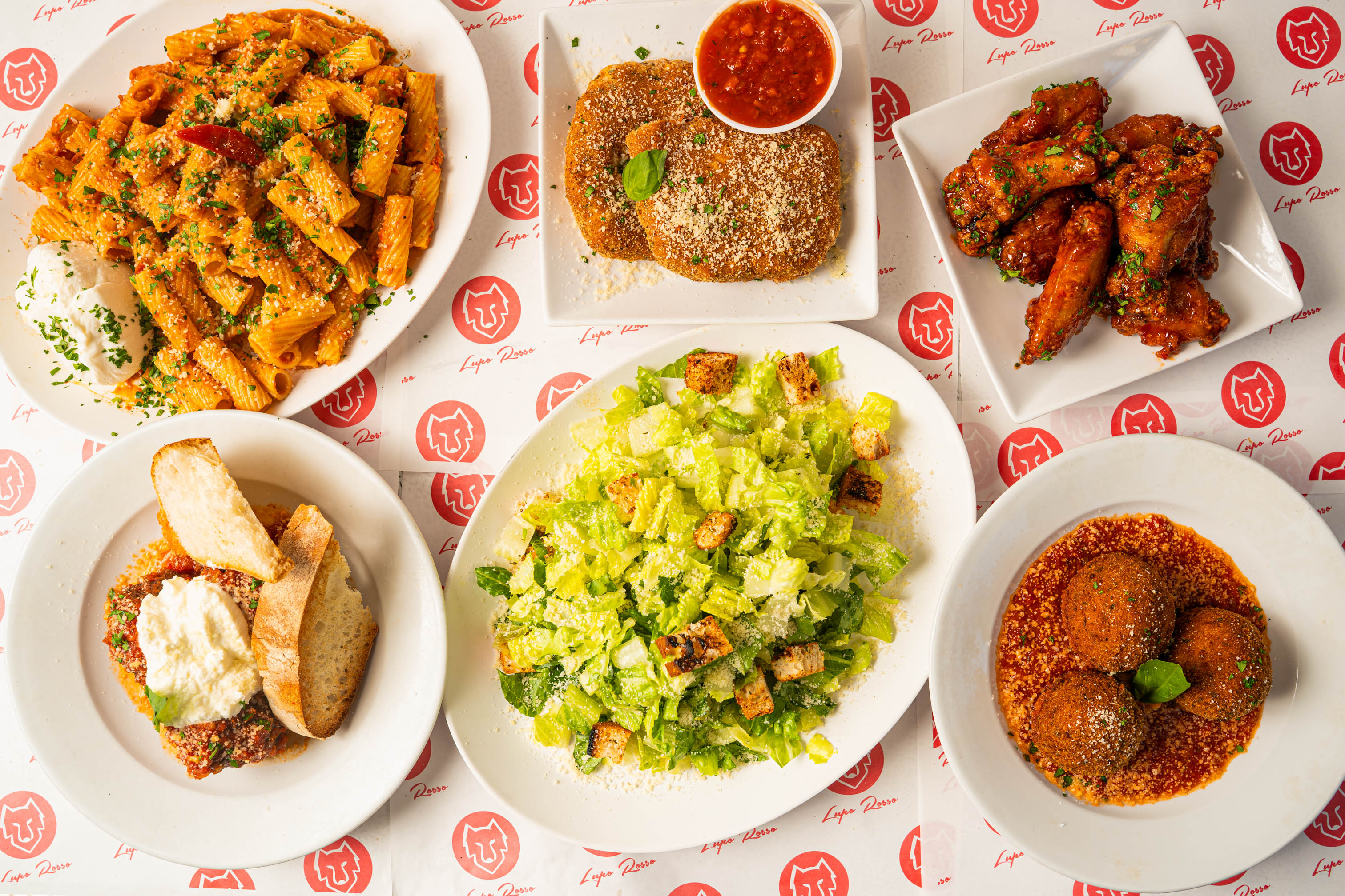Assorted dishes on a table including Caesar salad, pasta, chicken wings, and fried mozzarella cakes