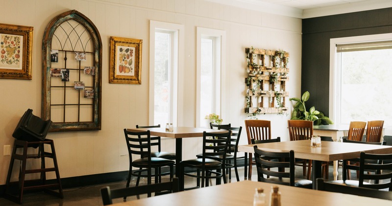 Interior - wooden tables & black chairs, a framed window with photos and artworks on the walls.