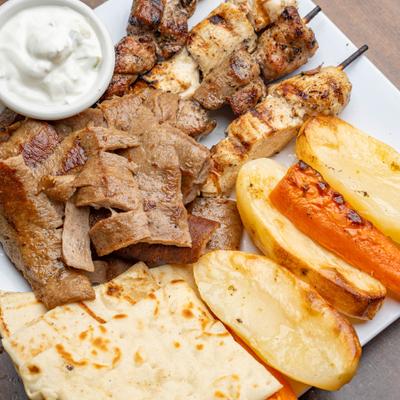 Greek combo platter with gyro, souvlaki, roasted potatoes, pita, and tzatziki.