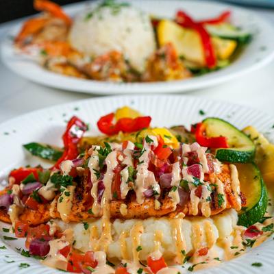 Grilled salmon with mashed potatoes, sauteed vegetables, and creamy sauce.