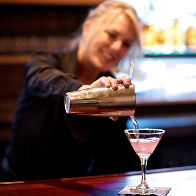 bartender pouring a light pink cocktail