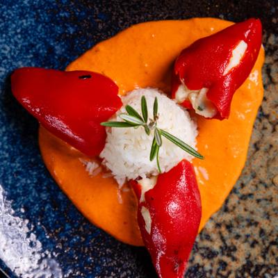 Spanish appetizer featuring roasted peppers filled with creamy cod, served over sauce with rice.