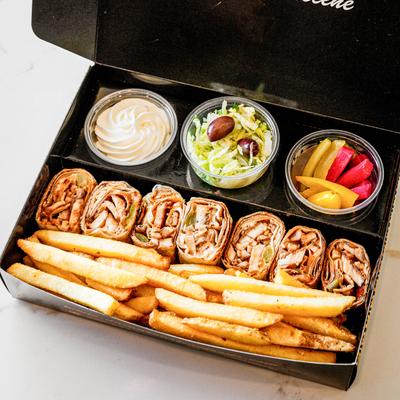 Shawarma, fries, pickles, salad, and a spread in a take out box.
