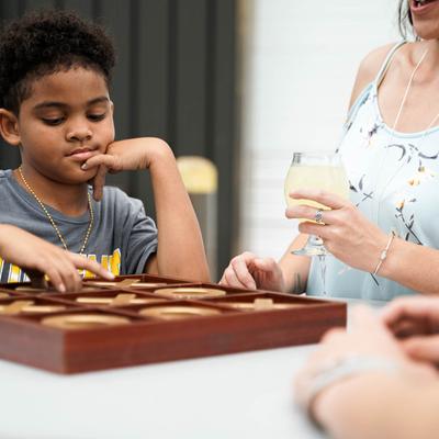 Young child playing a board game at a table outdoors.