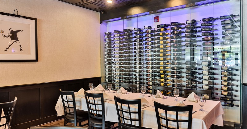 Restaurant interior, dining table set for eight guests, wine rack in the back