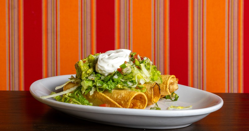 Chicken taquitos, topped with lettuce, tomato salsa, quacamole, and sour cream