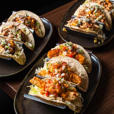 Assorted tacos with various toppings served on dark ceramic plates.