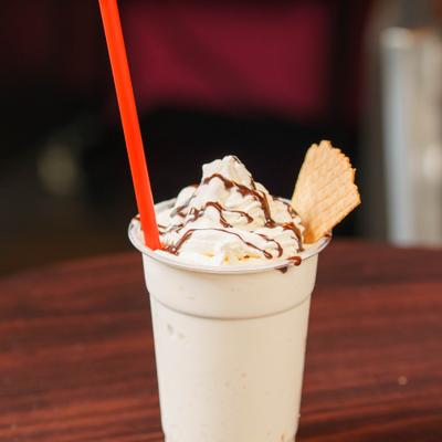Milkshake topped with whipped cream, chocolate syrup drizzle, and a waffle cone.