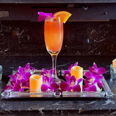 Mimosa in a classic champagne flute, served on a tray adorned with orchids and candles.