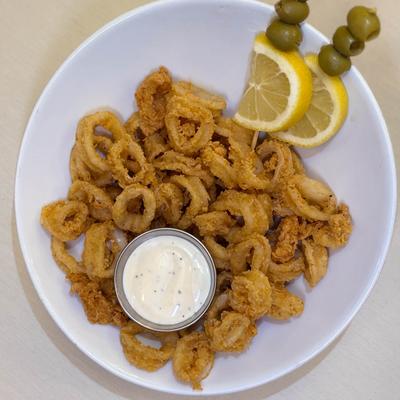 Fried calamari with dipping sauce, lemon slices, and olives.