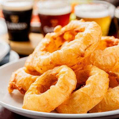 Onion rings with pints of beer in the background.
