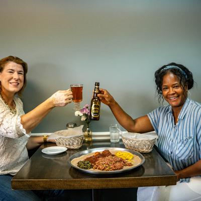 Two customers smile while toasting with drinks over a platter of Ethiopian food.
