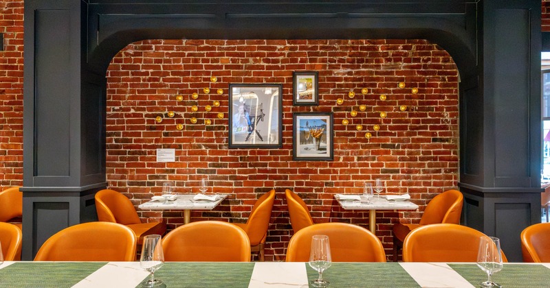 Restaurant interior with orange chairs, a marble countertop, and a red brick wall with framed art and decorative elements