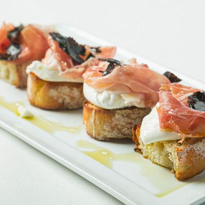 Crostini, with burrata cheese, black truffles, and prosciutto.