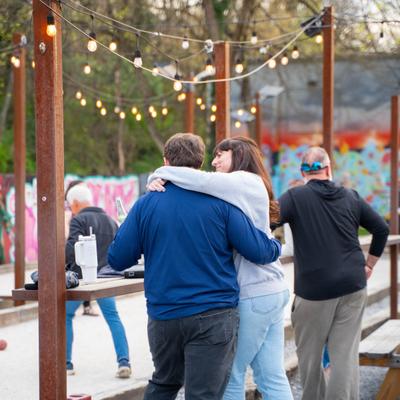 People playing bocce ball outdoors with string lights and graffiti in the background.