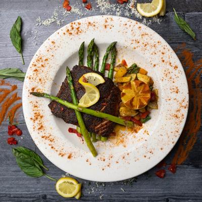 A white plate with blackened fish, two asparagus spears, and roasted vegetables.