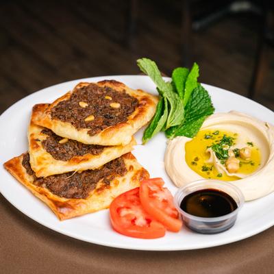 Lebanese meat pies on a plate with hummus, a sauce, fresh mint and tomatoes.