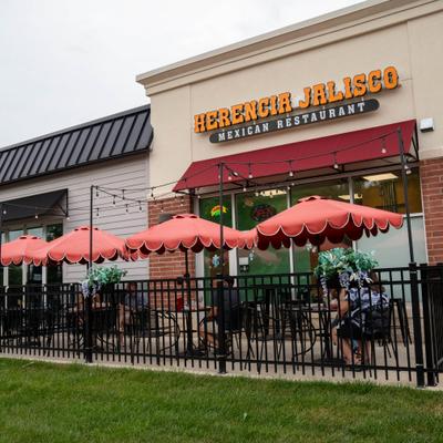 Storefront featuring outdoor seating with red umbrellas and a black metal fence.