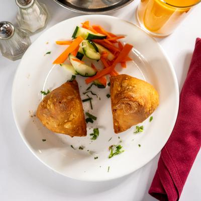 Two vegetable samosas served on a plate with fresh veggies.