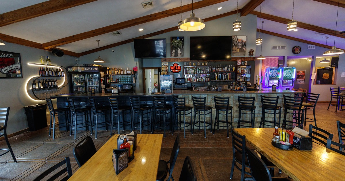 Bar interior with black stools, drink shelves, and gaming machines
