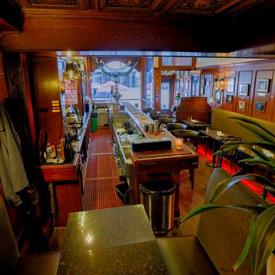 Restaurant interior with a bar, banquette seating, wooden walls, and wall art.