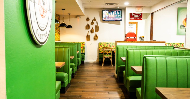 Interior of a restaurant with green booth seating and wooden tables, decoration and pendant lights
