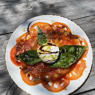A Burrata Caprese Salad on a rustic wooden table outdoors, top down view.