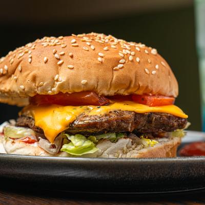 Beef burger with cheese, lettuce, and tomato, close up.