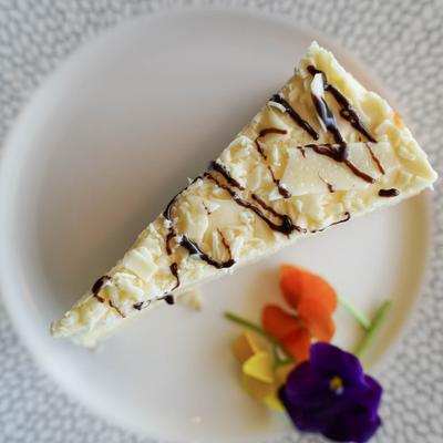 A slice of cheesecake, drizzled with chocolate sauce, served on a plate with flowers.