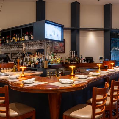Warmly lit restaurant bar with a wooden counter, stools, and place settings.