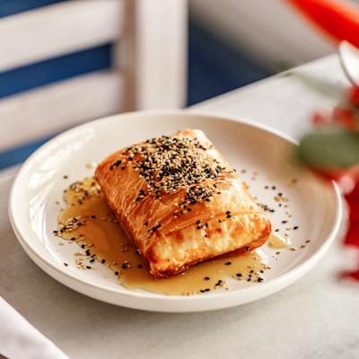 Greek feta  topped with sesame seeds is served on a white plate, drizzled with honey.